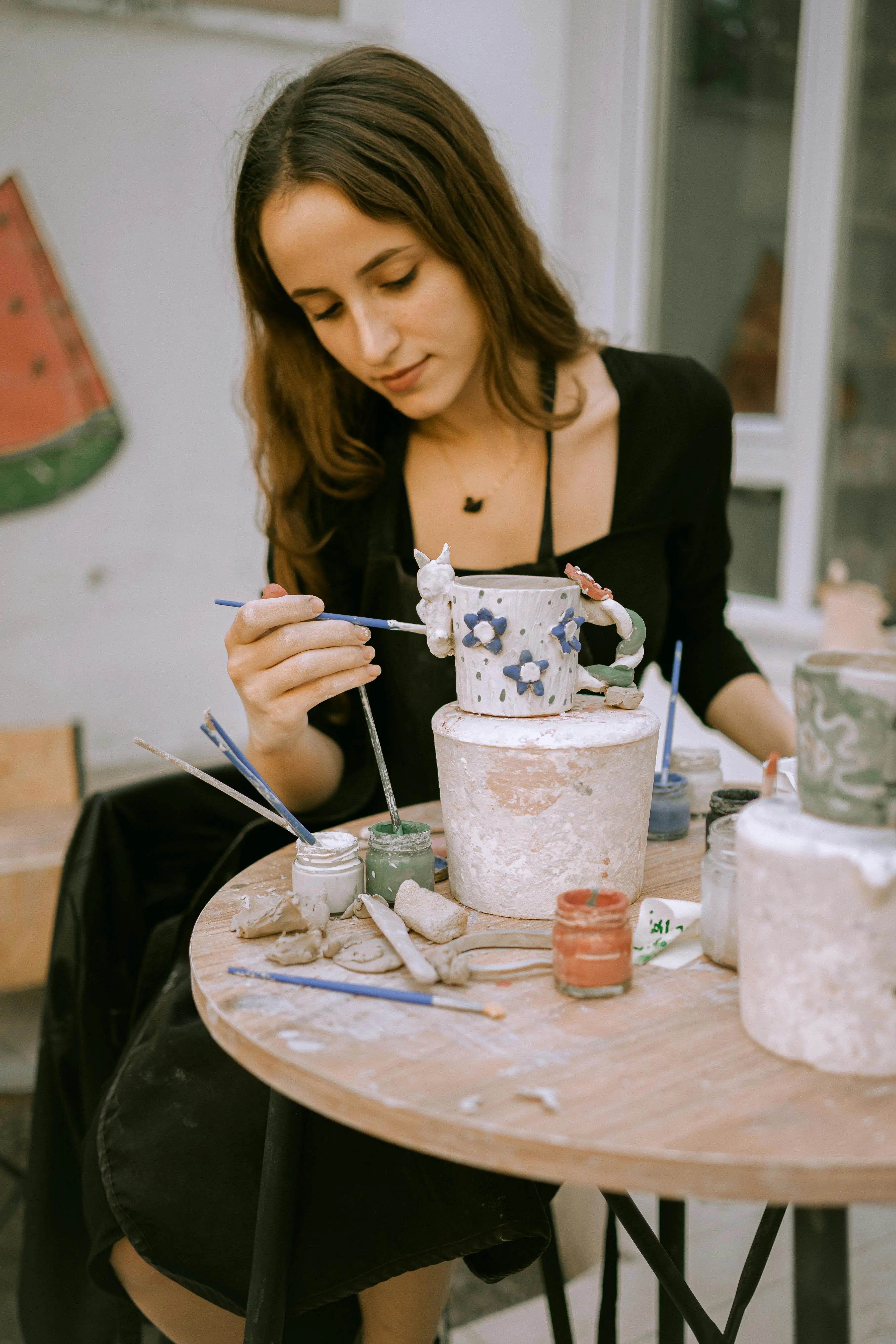 Gemeinsame Töpfer-Session mit Freunden: Frau verziert Keramikbecher mit DIY-Töpferset und Pinsel.