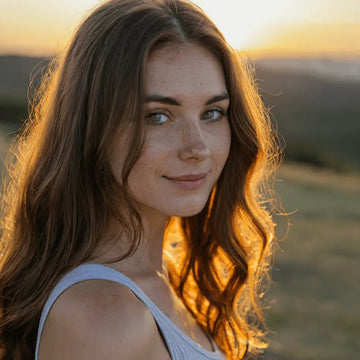 Junge Frau mit Sommersprossen im goldenen Abendlicht, die nach gemeinsamer DIY-Töpferset-Session entspannt an einem Feldrand spazieren geht.